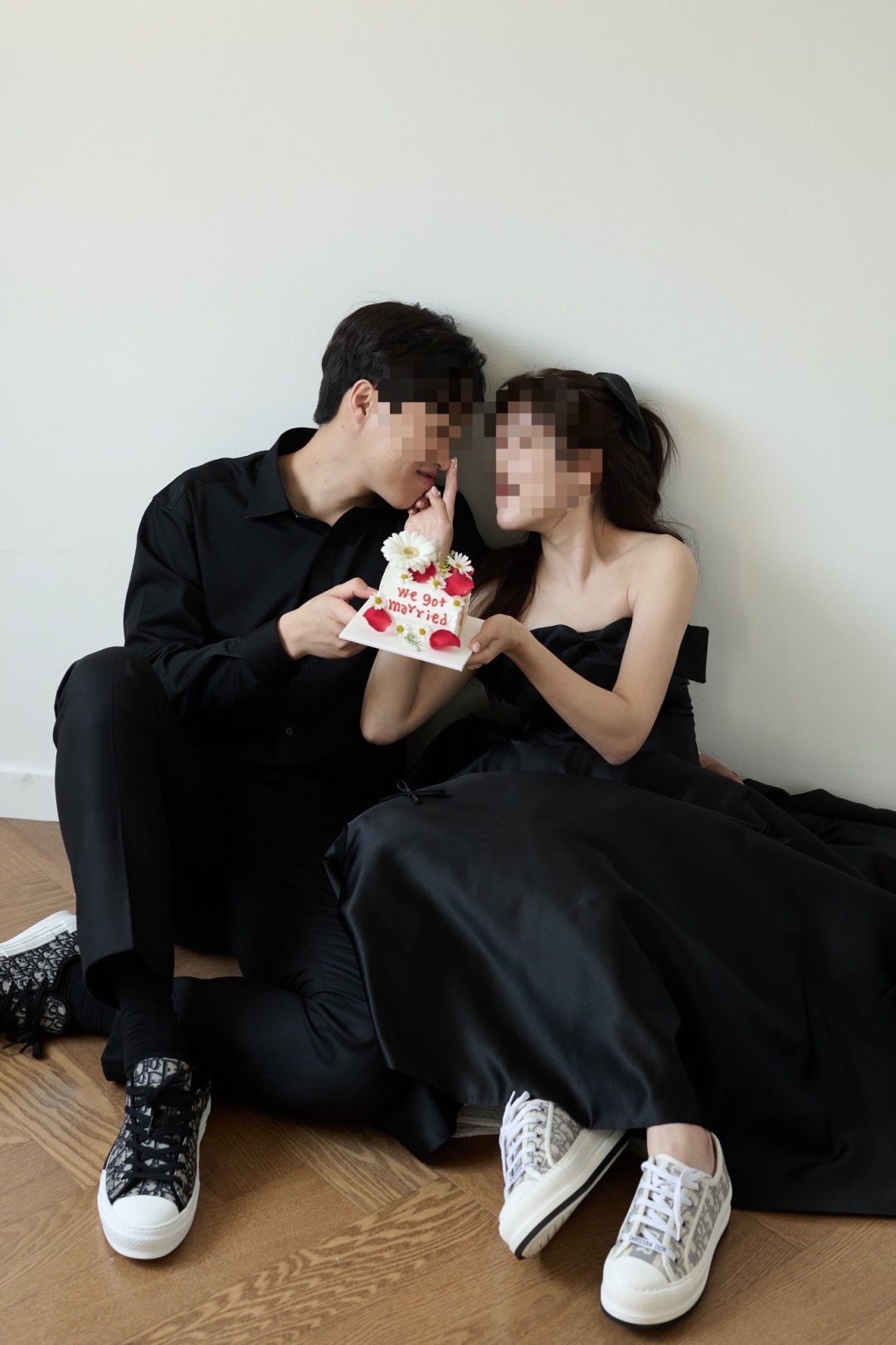 올블랙 셔츠와 원피스에 커플 운동화를 신고 바닥에 앉아 케이크를 먹여주는 스튜디오 캐주얼 컷이에요. 블랙 리본 반묶음으로 포인트를 줬어요.