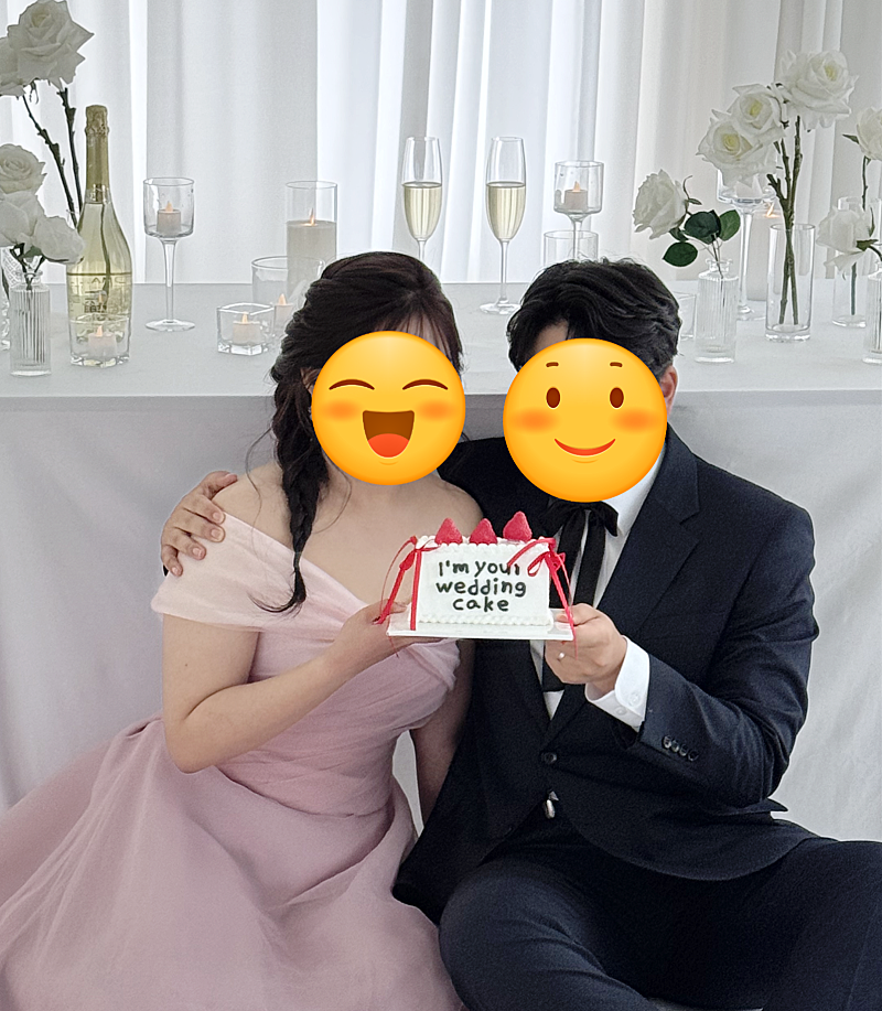 핑크 드레스 신부와 신랑이 케이크를 들고 앉아 있고 뒤 테이블에 샴페인 잔과 병이 깔린 컷이에요. 잔에는 데미소다를 부었다고 해요.