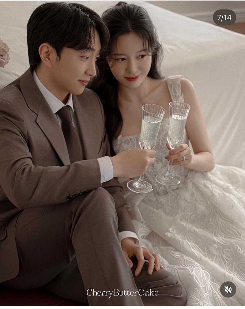 침대에 기대 앉아 둘이 샴페인 잔을 부딪치는 실내 건배 컷이에요. 작성자가 모은 스튜디오 시안이에요.
